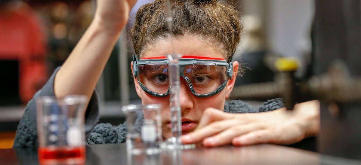 Closeup of student wearing safety goggles dropping liquid into a test tube