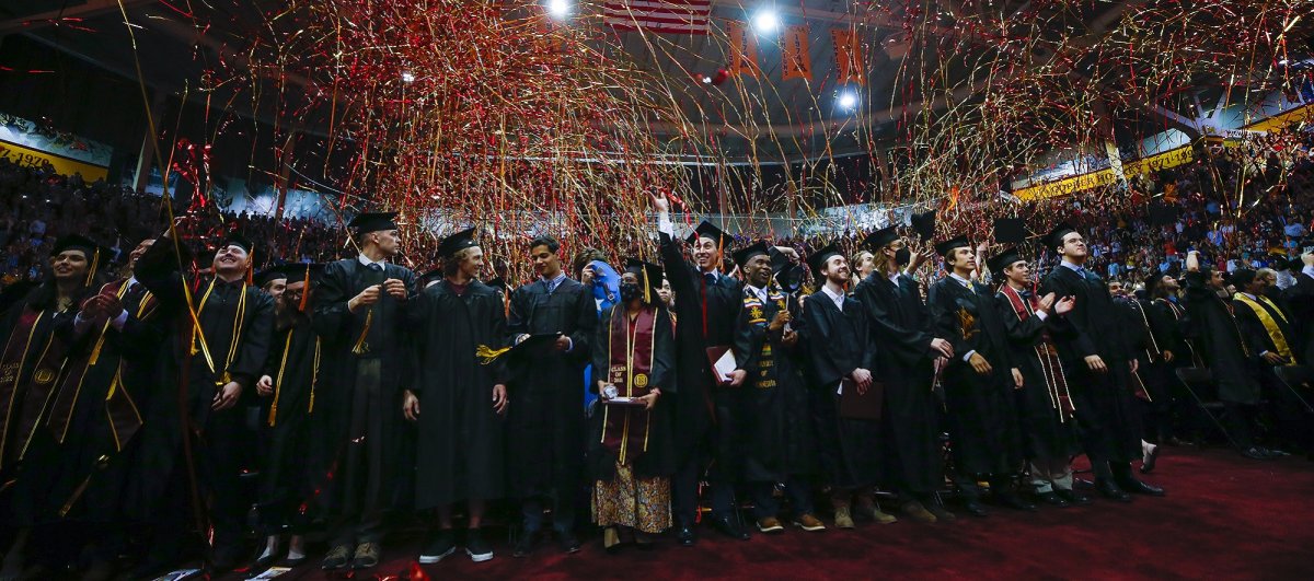 Students in graduation regalia celebrating indoors in Mariucci arena