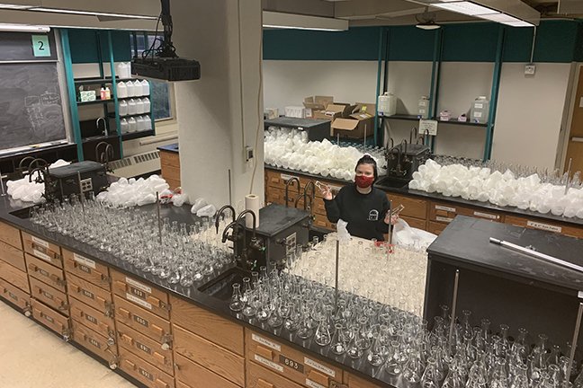 Student in lab surrounded by boxes and glass vials