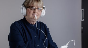 Woman wearing headphones and with device in mouth as part of tinnitus treatment
