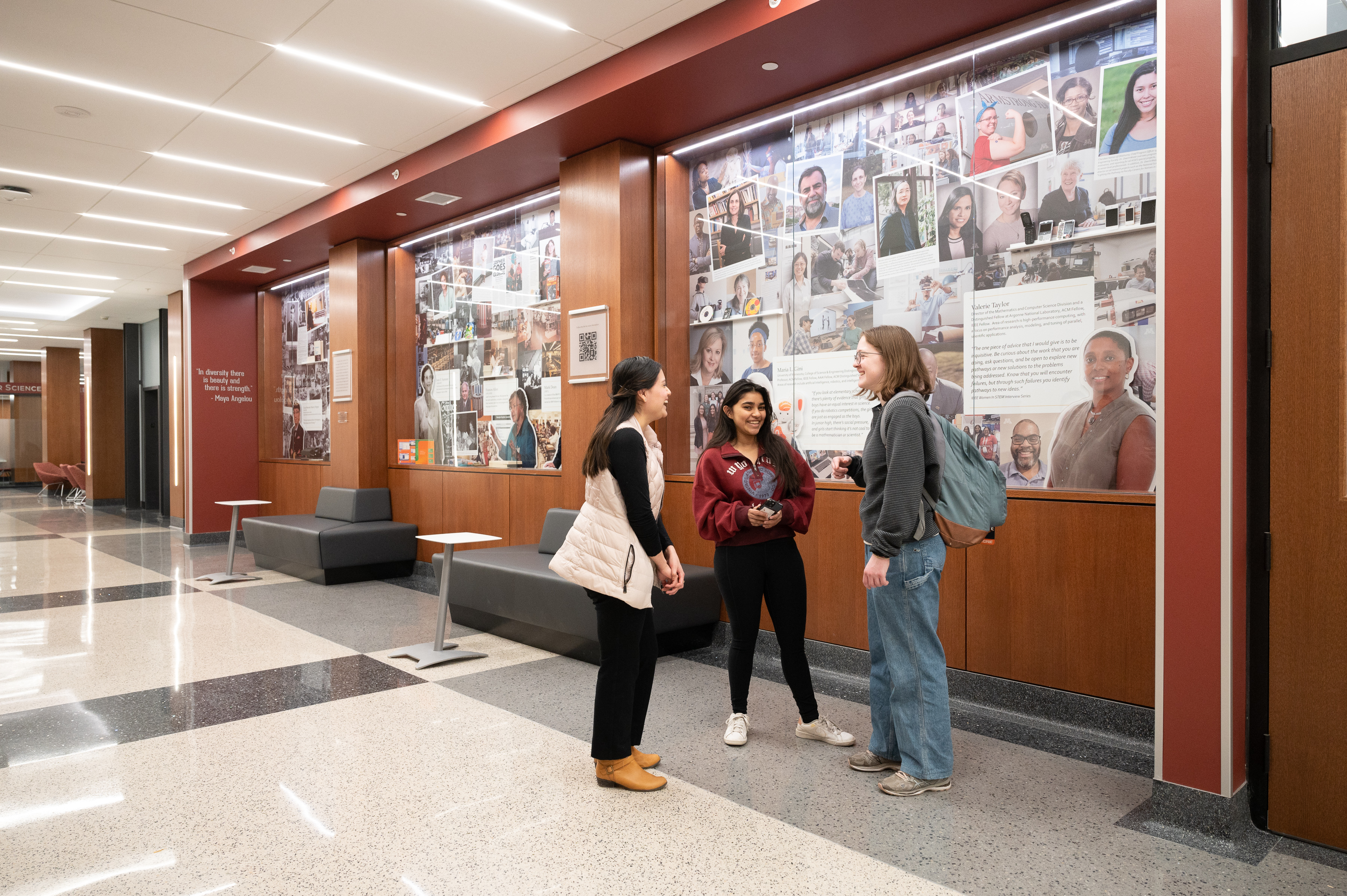 Three female students talk in front of the Lind Hall Diversity Wall