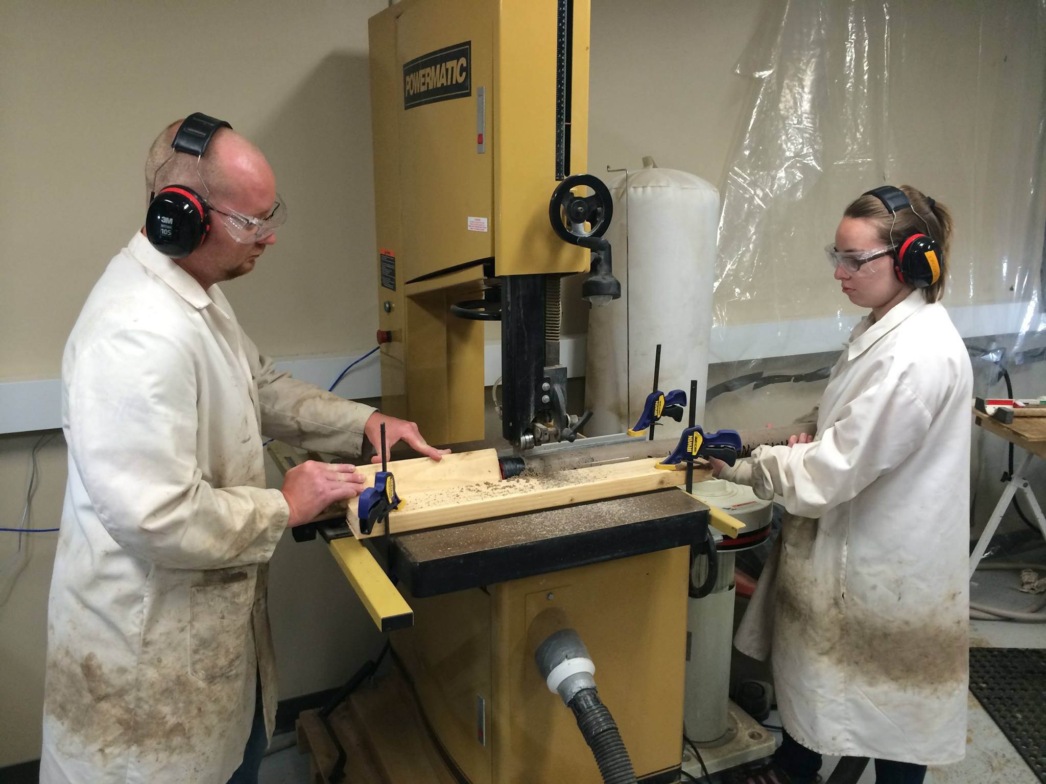 Two people passing a core through a bandsaw.