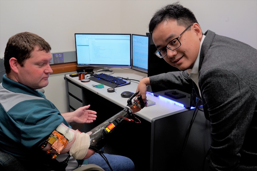 Research participant Cameron Slavens shaking robotic hands with CSE Professor Zhi Yang