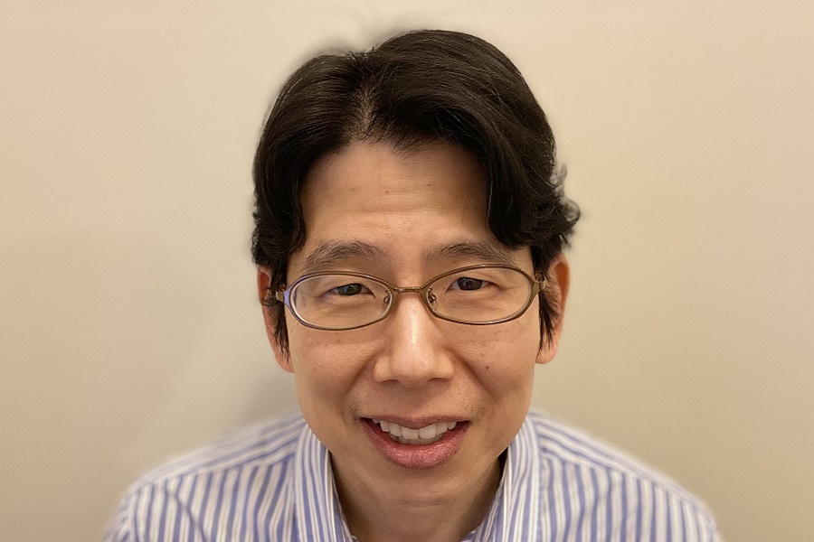 Professor Chris Kim wearing a striped blue and white shirt against a yellow background