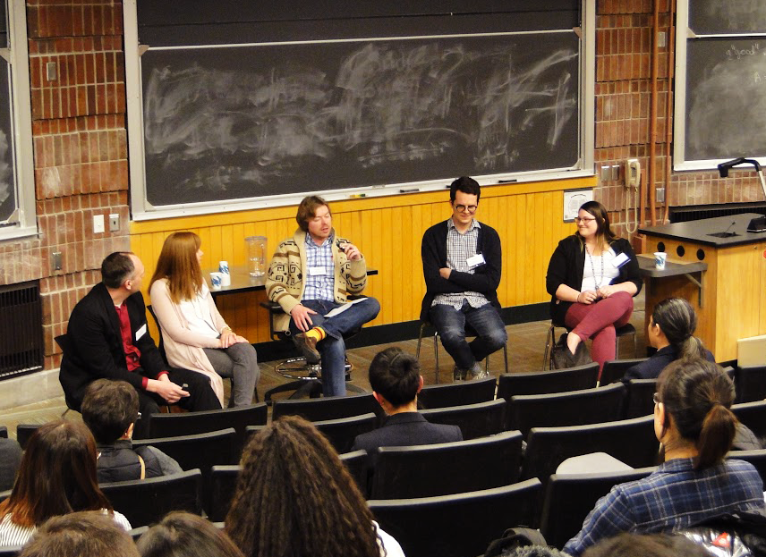 Five speakers presenting to an auditorium of students.