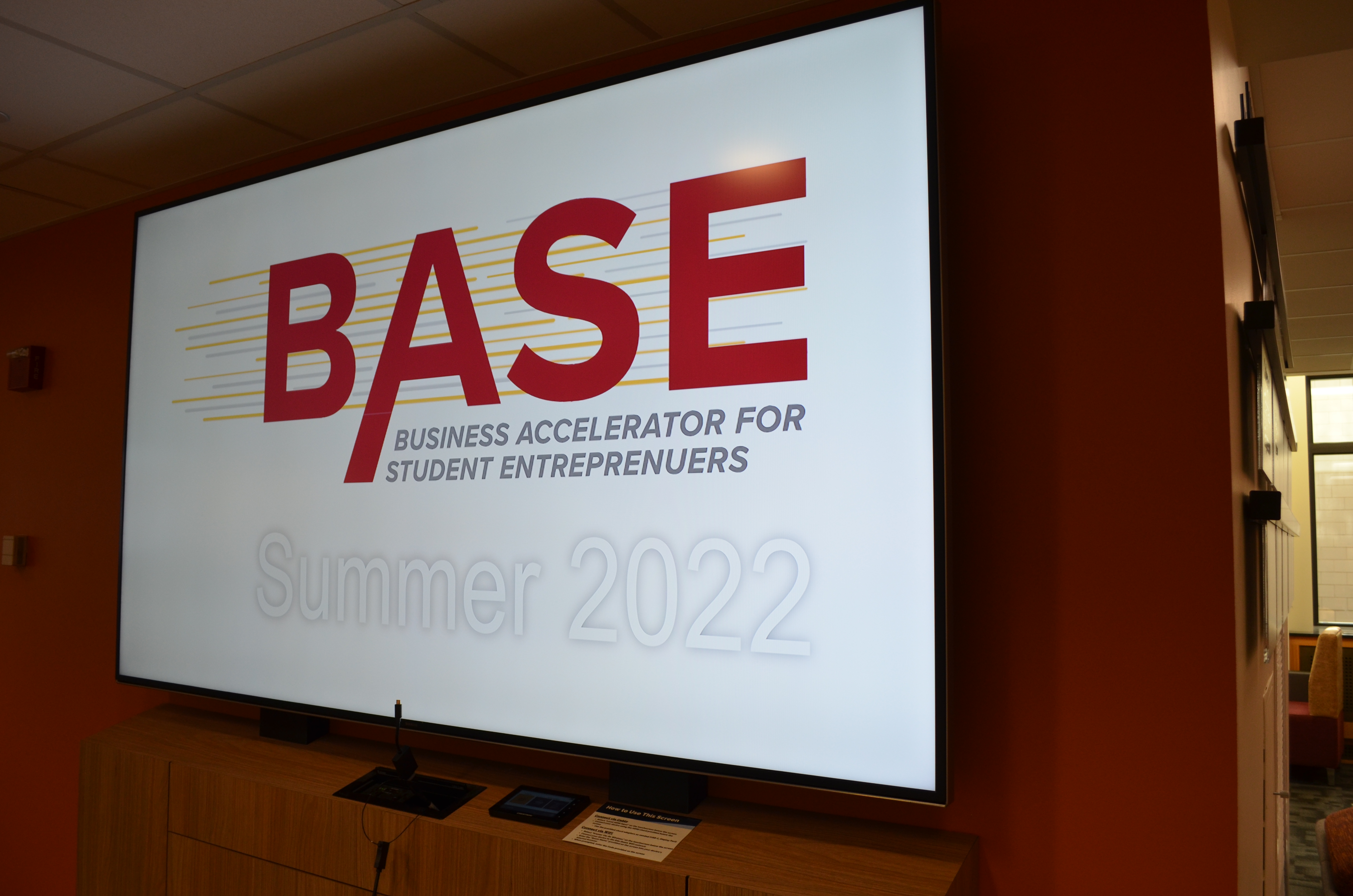 An illuminated screen reads BASE: Business Accelerator for Student Entrepreneurs