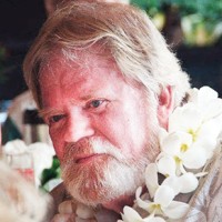 bearded man with gray hair wearing a Hawaiian lei of white flowers