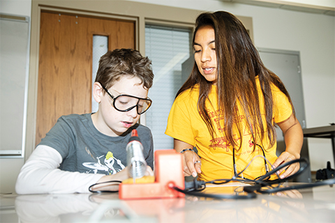 Mechanical engineering junior Keila Cortes teaches a student how to solder circuits last summer.