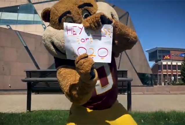 Goldy Gopher holding a sign that says "Hey Class of 2020" outside of the McNamara Alumni Center