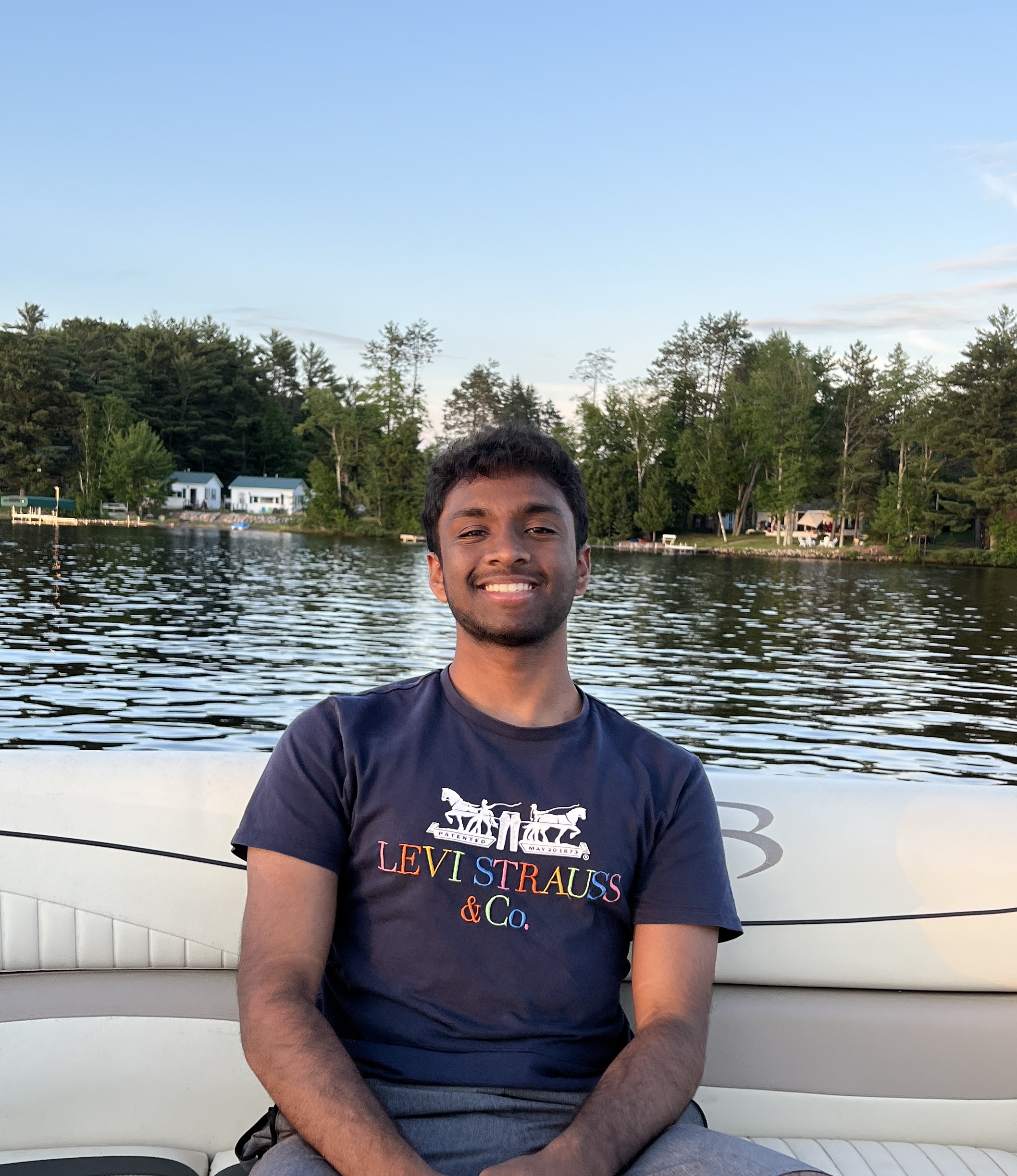 Akshay Peddi poses on a boat on a lake with trees in the background