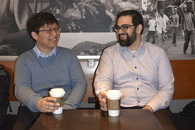 A student and his professor sitting with coffee cups in their hands.