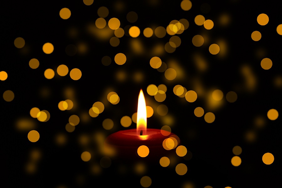 A single lit red candle against a background of diffused lights