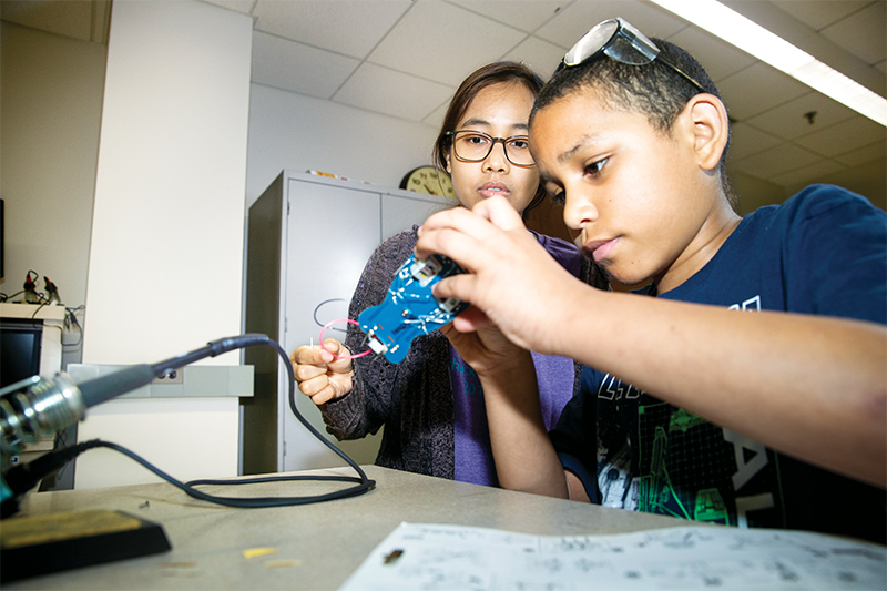 Computer science grad student Myat Mo guides a middle school student in building a robotic bug. 