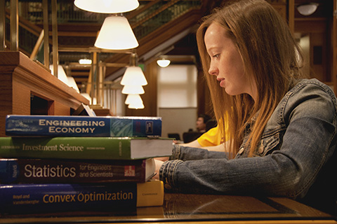 student with stack of books studying in library