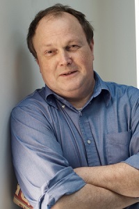 Michel Janssen crossing arms, wearing a blue, button-down shirt with sleeves rolled up to his elbows