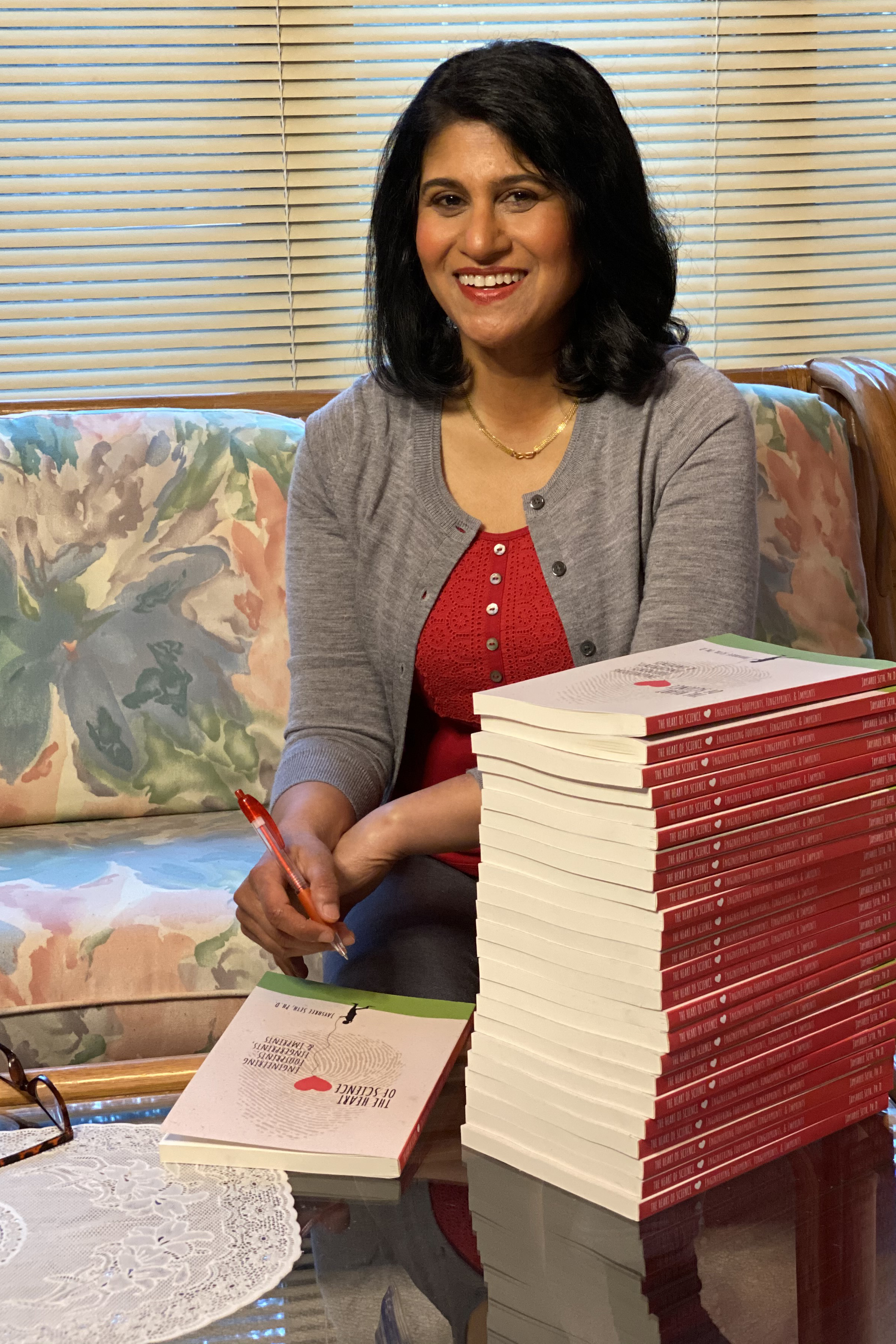 Jayshree Seth with a pen in hand, sitting next to a stack of her books.