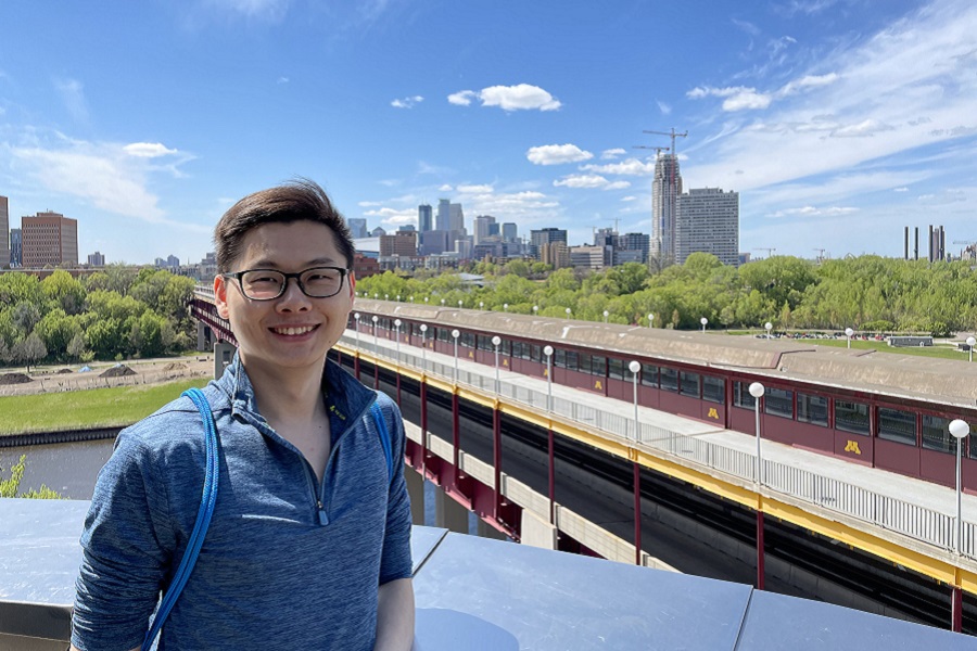 Kai Wu standing on pedestrian bridge across from Coffman Memorial Union with his back to downtown Minneapolis