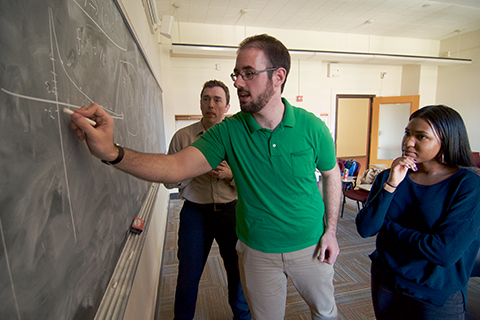 Faculty and students writing on a chalkboard