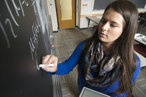 Student at blackboard writing equations.