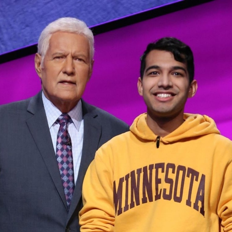 Student Nibir Sarma wearing a Minnesota sweatshirt standing next to host Alex Trebek in the set of Jeopardy!