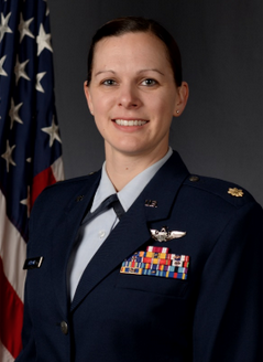 An air force major in dress uniform standing in front of an American flag