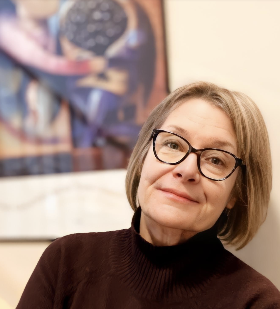 A woman in glasses, with a painting in the background