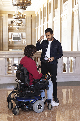 Stephen Mylabathula demonstrating a headband to a man in a wheelchair.