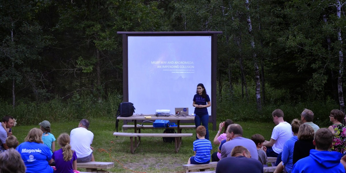 A student standing in front of an outdoor screen with people watching her. 