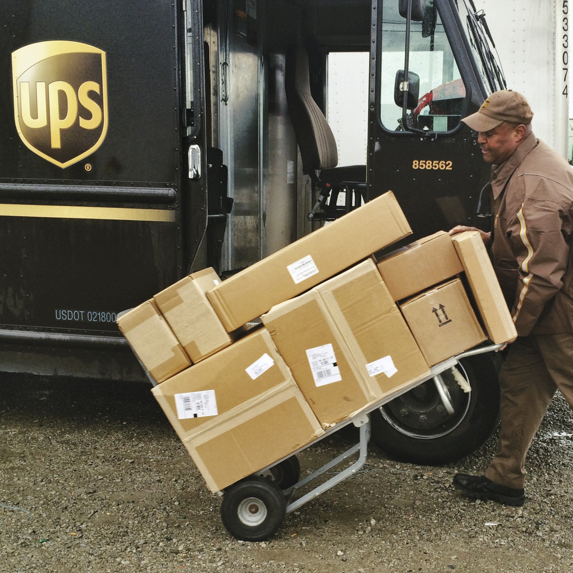 UPS driver pushing boxes on a dolley, in front of the UPS truck