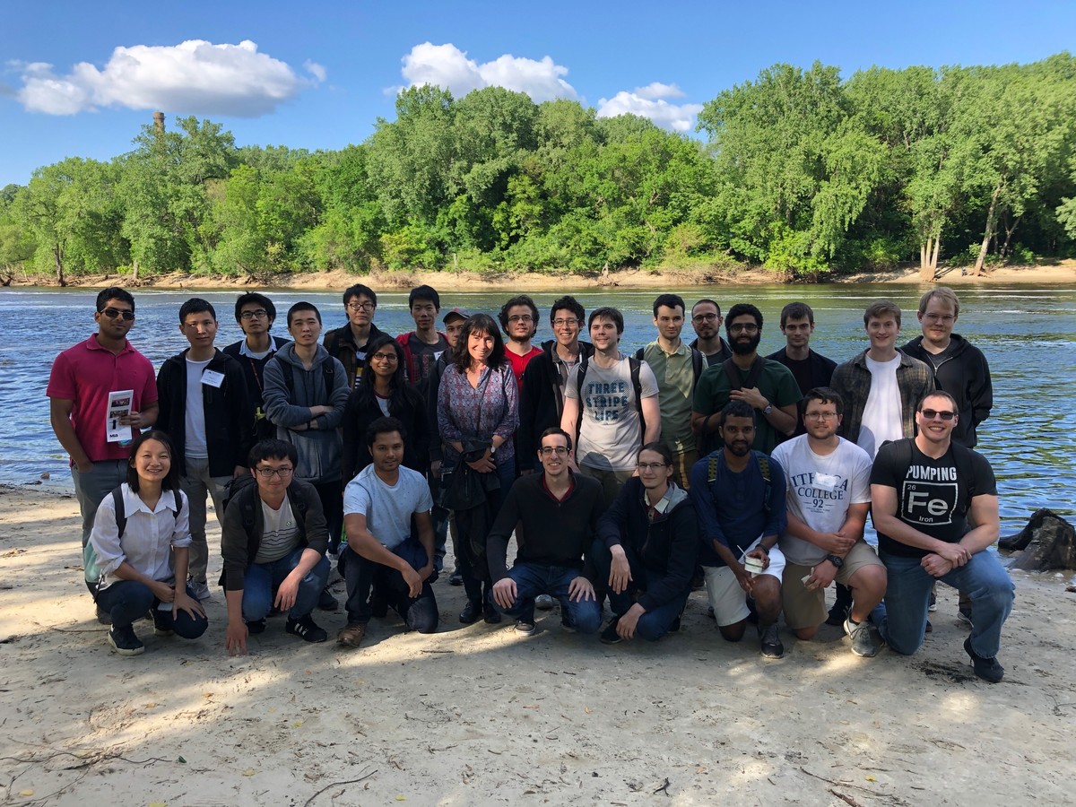 group of theoretical physicists standing together in front of the mississippi river on a sunny day
