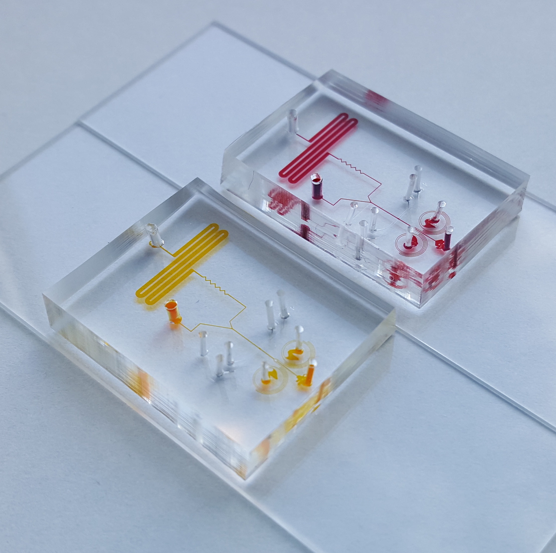 Medical devices from the Living Devices Lab. Two clear devices; one with red lines and one with yellow.