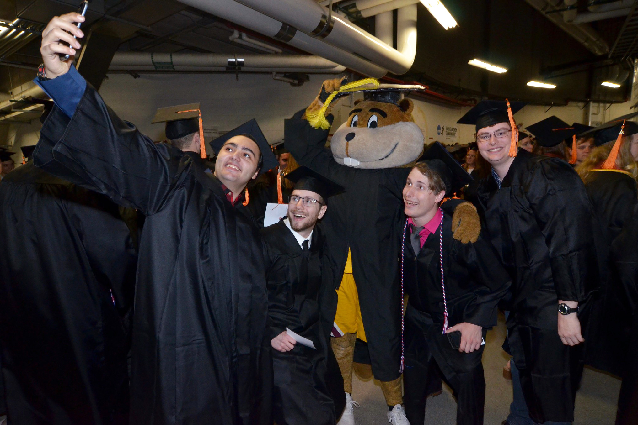Four students posing for a photo at graduation with Goldy Gopher.