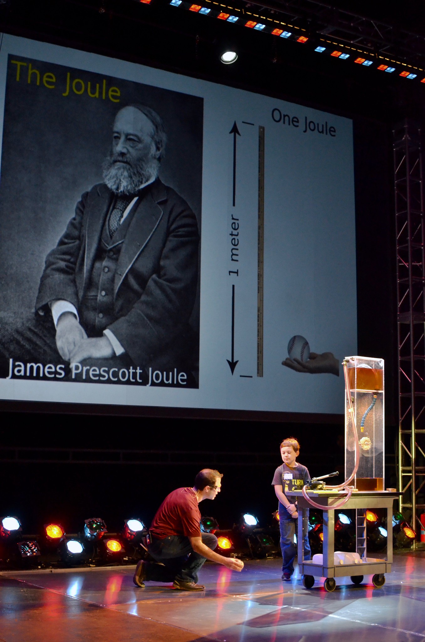 A boy on stage watching a professor explain an experiment.
