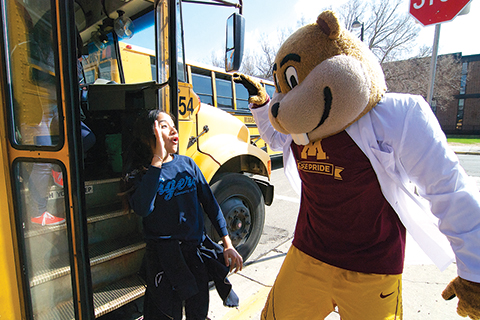 Goldy high-giving a student getting off the bus