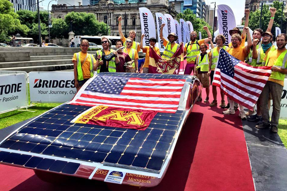 solar car team posing with car draped in UMN and US flags