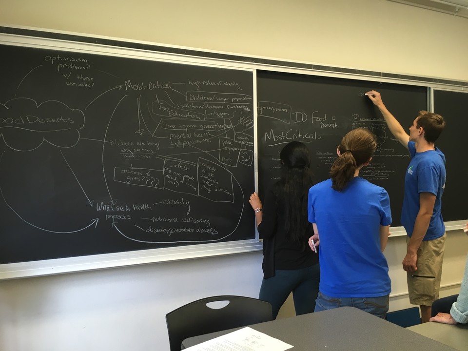 Instructor and two students at board at Math Modeling Camp