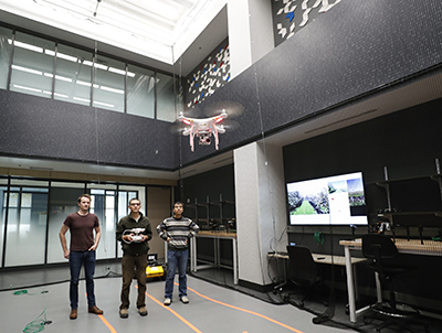 Three students flying a drone inside a two-story room.