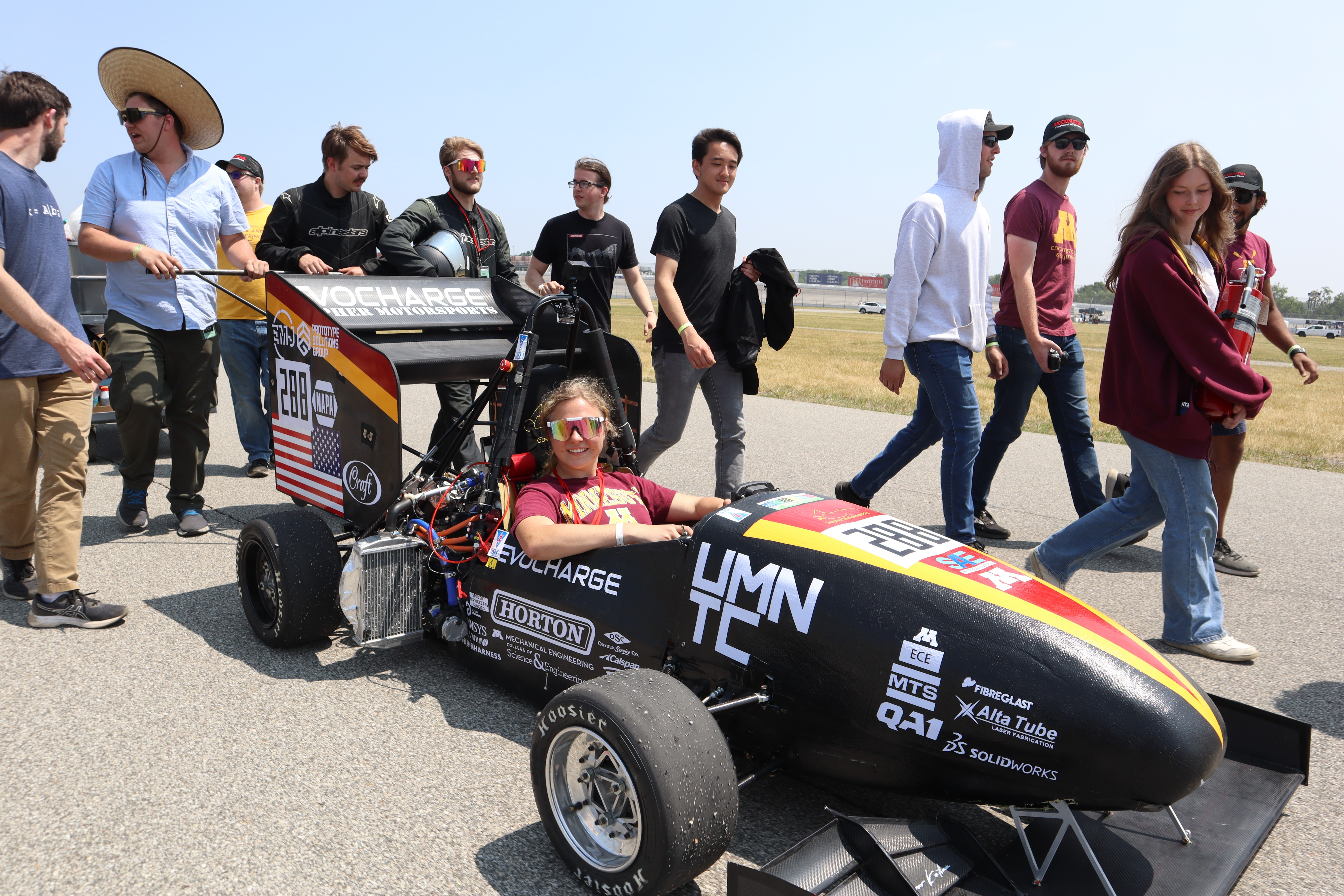 image of female student in solar vehicle with team behind her