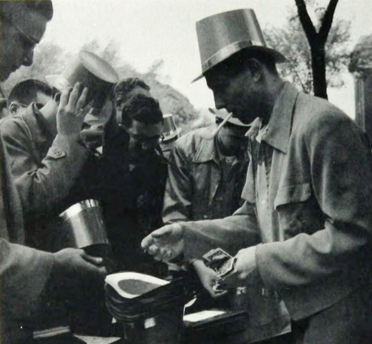 In 1953, A huckstering engineer sells traditional green hat, clenches a clay pipe in his teeth. Hats help separate genuine IT men from crowds attending ceremonies