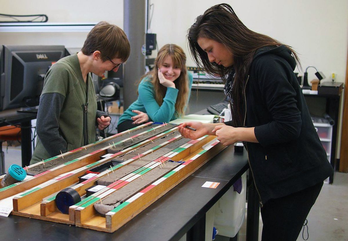 Three female technicians examine and take samples from a core
