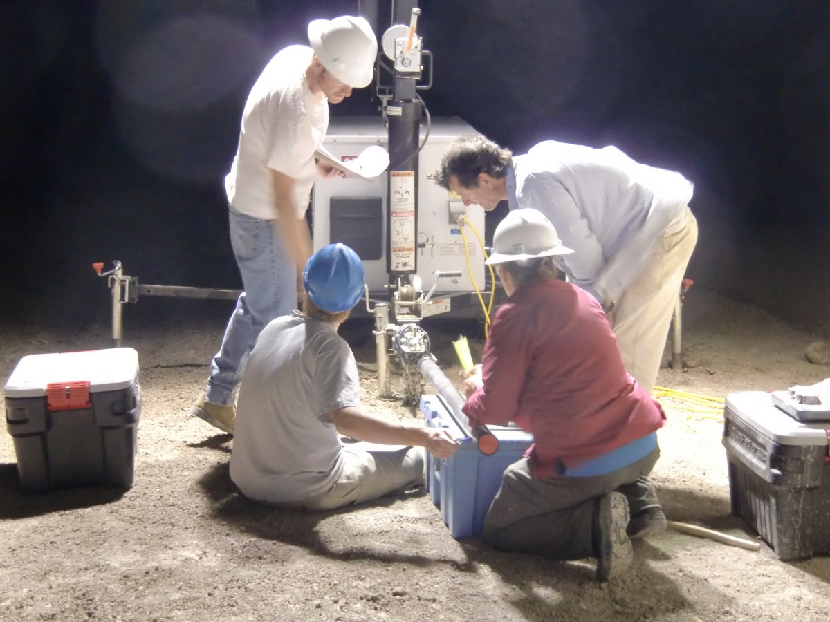 Four scientists examine a new core as it emerges during night time drilling