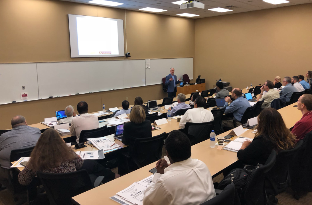 TLI Gemini Chair Kirk Froggatt addressing a large group of attendees at a Rochester Signature Series event, in a large lecture hall
