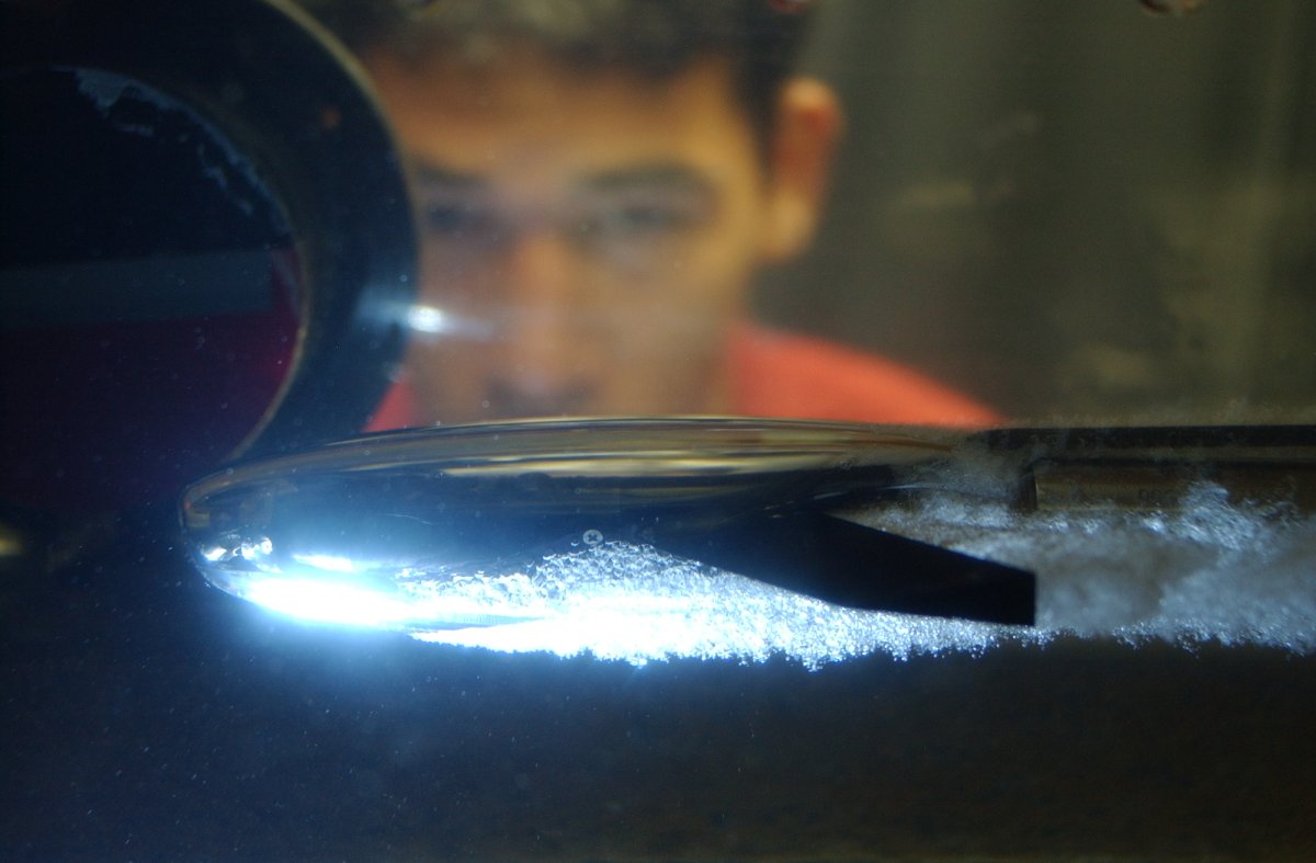 Photo of a torpedo shaped object moving through the water tunnel while a researcher watches