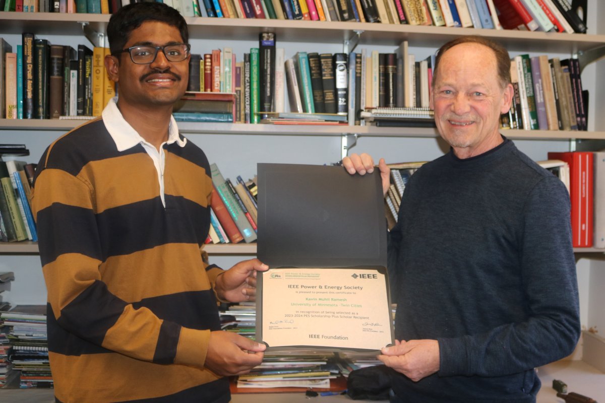 Kavin in yello and black striped shirt receiving award certificate from Professor Paul Imbertson who is wearing a navy sweater