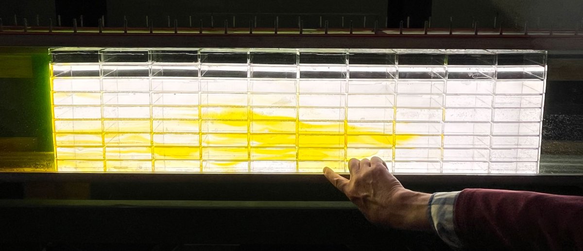 An illuminated water flume in a dark room, with yellow dye moving through