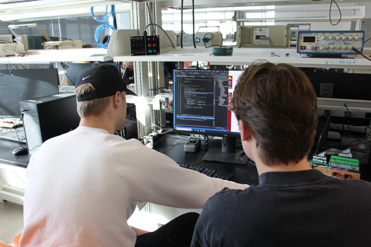 students with backs to camera work at a computer in a lab setting