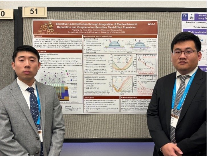 Two students stand in front of a research poster wearing suits and ties