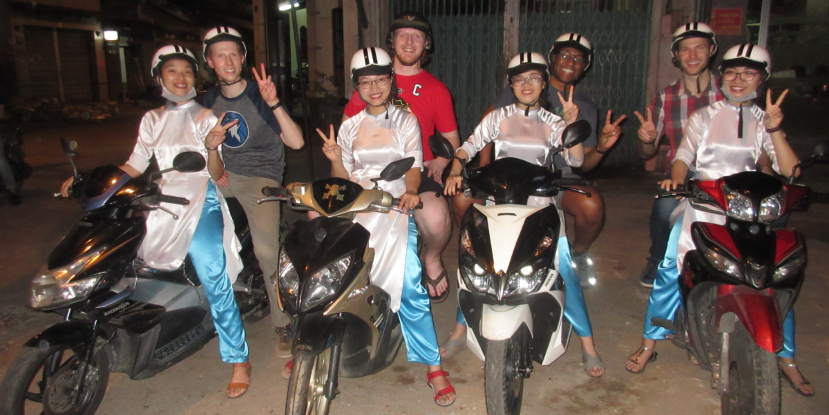 Four MOT students and their four respective tour guides seated on mopeds as part of their gastronomy tour in Ho Chi Minh City, Vietnam