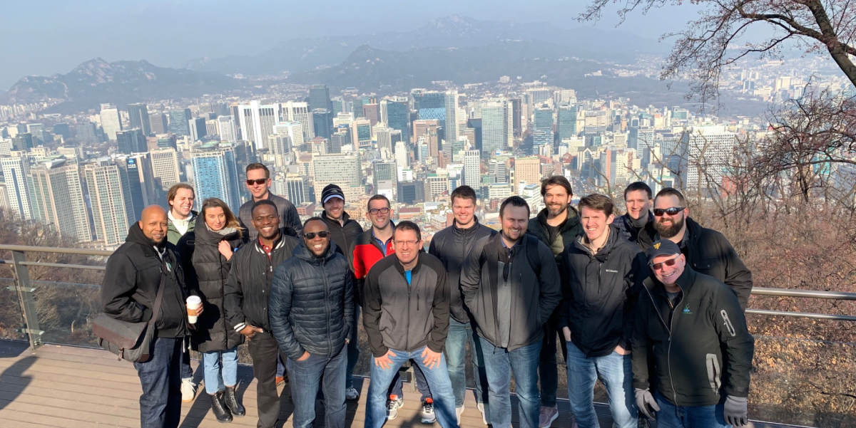 MOT students, donning cold weather gear, at an overlook on a sunny day with skyline of the city of Seoul in the background.