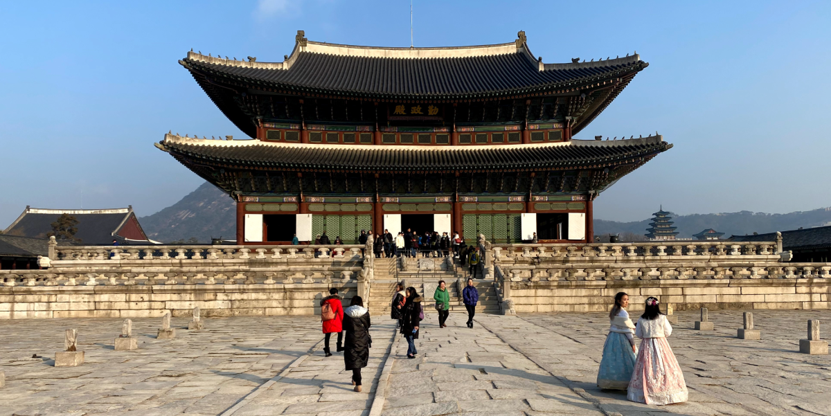 A temple in Seoul, South Korea with few tourists and locals in traditional attire wandering about the plaza in front of it.